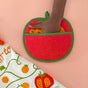 A hand slips into The Neighborgoods Pot Holder - Tomato on a peach background. Next to it is a white cloth with orange and green tomato illustrations—an eye-catching kitchen essential.
