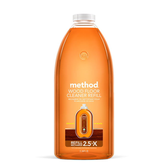 A clear bottle of Method Wood Floor Cleaner Refill in almond scent, filled with orange-brown liquid. The label displays product information and highlights that it is a 2.5x refill for wood floor cleaning.