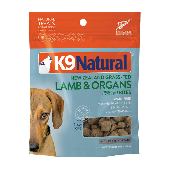 A bag of K9 Natural dog treats labeled “New Zealand Grass-Fed Lamb & Organs Healthy Bites.” The packaging is blue and orange, featuring a dogs face and images of the treats.