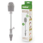 The Haakaa Double-Ended Silicone Cleaning & Bottle Brush, from a versatile set, is next to its green and white box featuring product details and illustrations. It has a round, spiky end and a narrow, textured handle, ideal for cleaning essential baby gear.