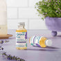 Two small bottles of Grove Co. multi-purpose cleaner concentrate with lavender blossom and thyme are placed on a lavender-colored surface, with lavender sprigs and a potted plant in the background.