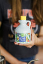 A person holding a small white jug with a yellow cap labeled Plant Food featuring a colorful illustration of fruits and vegetables on the label. The persons face is not visible.