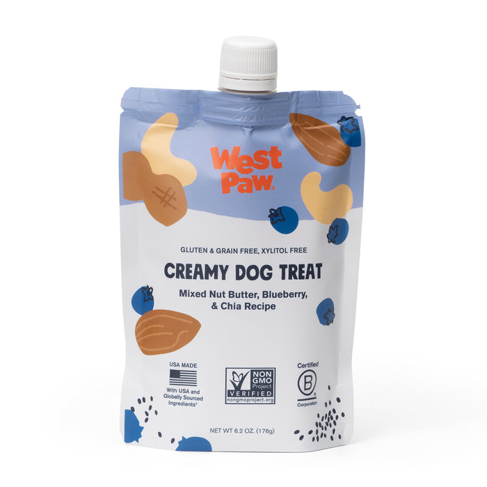 A stand-up pouch of West Paw Creamy Dog Treat, featuring mixed nut butter, blueberry, and chia recipe. The packaging is blue and white with images of nuts and blueberries, and displays various certifications and labels.