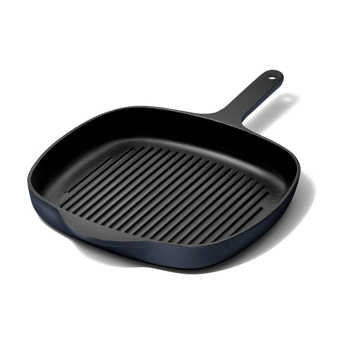 A black, square-shaped grill pan with a handle and ribbed cooking surface is placed on a white background, casting a soft shadow.