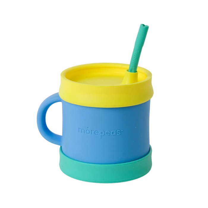 A blue silicone cup with a handle, green base, and yellow lid with a green straw inserted. The word morepeas is embossed on the side of the cup. The cup is isolated on a white background.