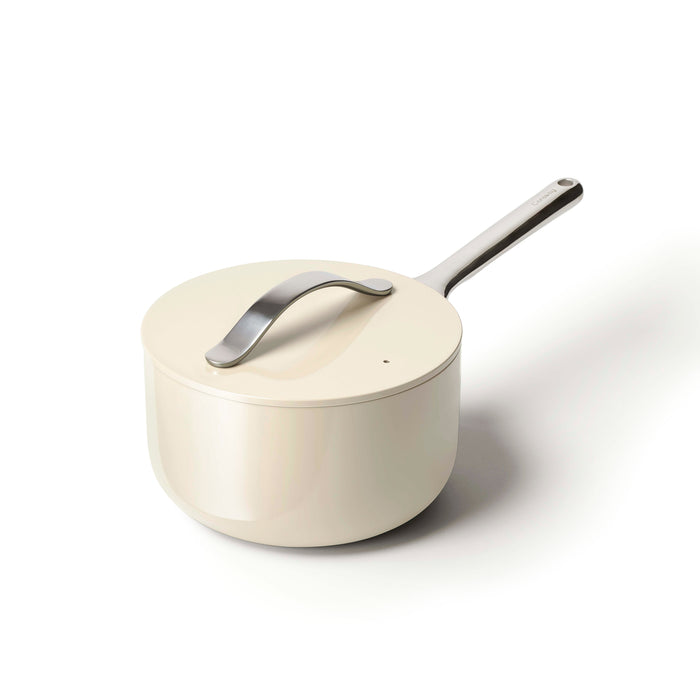A cream-colored saucepan with a matching lid and a long silver handle is shown on a white background. The pot has a modern, minimalist design.