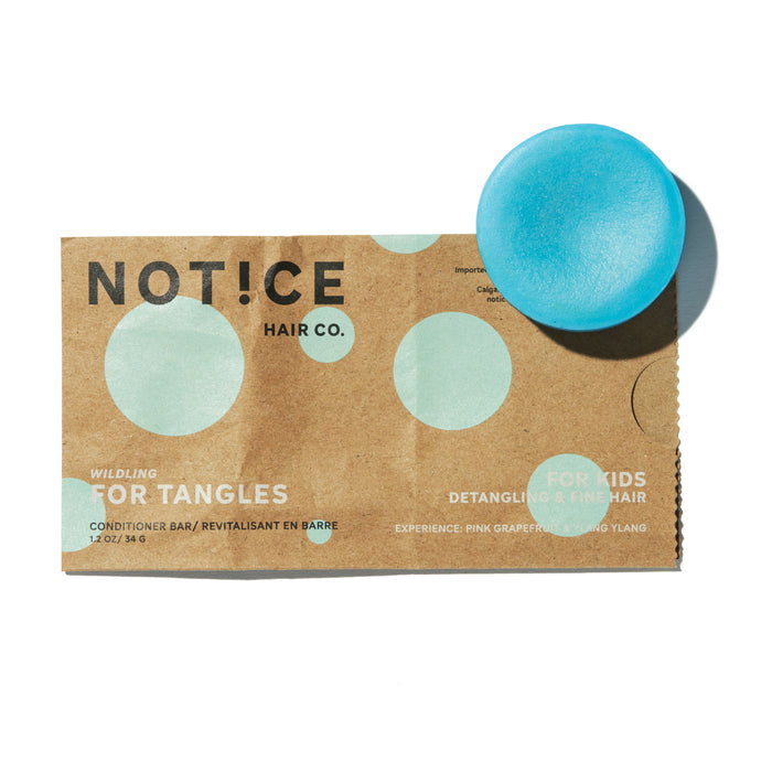 A small blue conditioner bar rests on top of a brown paper packet labeled NOT!CE Hair Co. Wildling For Tangles Conditioner Bar, designed for kids with detangling and fine hair benefits.