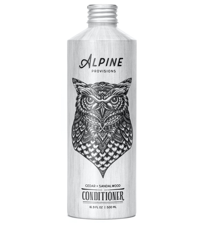 A silver bottle of Alpine Provisions conditioner featuring a detailed black illustration of an owl on the front. The label indicates cedar and sandalwood scent, with a 500 ml (16.9 fl oz) capacity.