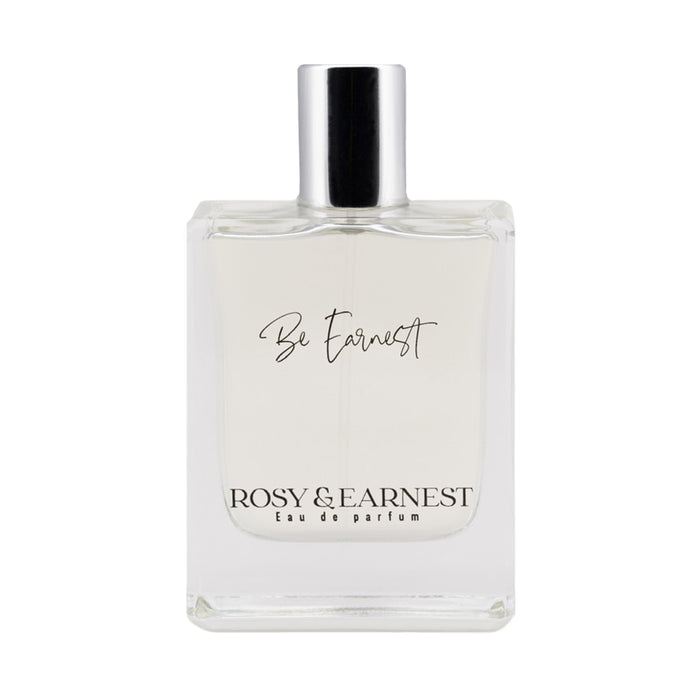 A clear glass perfume bottle with a silver cap, labeled Be Earnest on the front, and Rosy & Earnest Eau de parfum written at the bottom. The liquid inside appears nearly colorless.