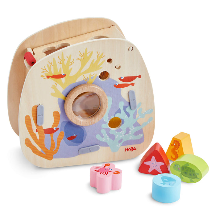 The Underwater World Wooden Shaper Sorter Toy by HABA features an underwater scene with various colorful sea-creature blocks resting in front.