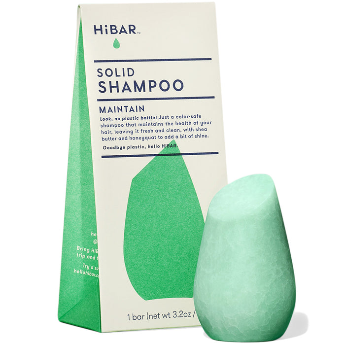 A green, uniquely-shaped solid shampoo bar stands in front of its upright, triangular HiBAR packaging labeled Solid Shampoo Maintain. The packaging highlights its eco-friendly, plastic-free design.