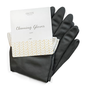 A pair of black cleaning gloves is partially covered by a white cardboard label with gold chevron patterns. The label reads Grove Co. and Cleaning Gloves, 1 pair. These durable latex gloves have textured fingertips and a soft lining inside.