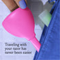A hand with purple nail polish holds a pink razor case embossed with "billie" near a blue zippered bag. Text reads, "Traveling with your razor has never been easier.