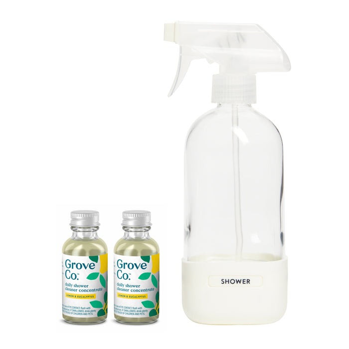 Two small bottles labeled Grove Collaborative daily shower cleaner concentrate sit beside a clear spray bottle with a white cap and base labeled SHOWER, all featuring a leaf design.