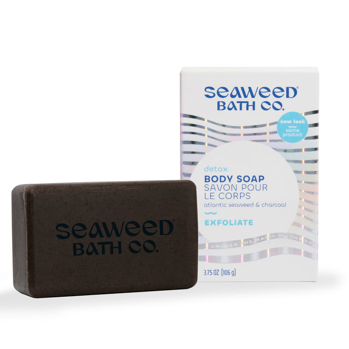 A brown rectangular bar of soap labeled Seaweed Bath Co. sits in front of its white box, which reads Detox Body Soap and lists Atlantic seaweed and charcoal as ingredients. The box features blue and silver accents.