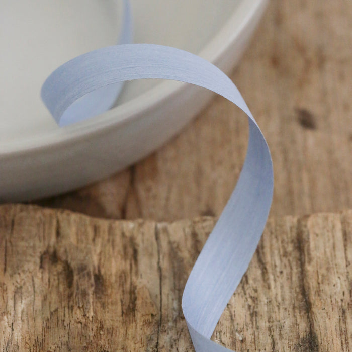 A pale blue paper ribbon curled on a rustic wooden surface, with part of a white ceramic bowl visible in the background.
