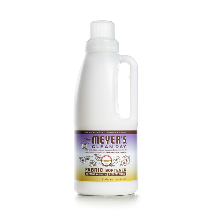 A bottle of Mrs. Meyers Clean Day Fabric Softener with a white cap and handle, featuring a purple and brown label with text and illustrations of flowers and leaves.