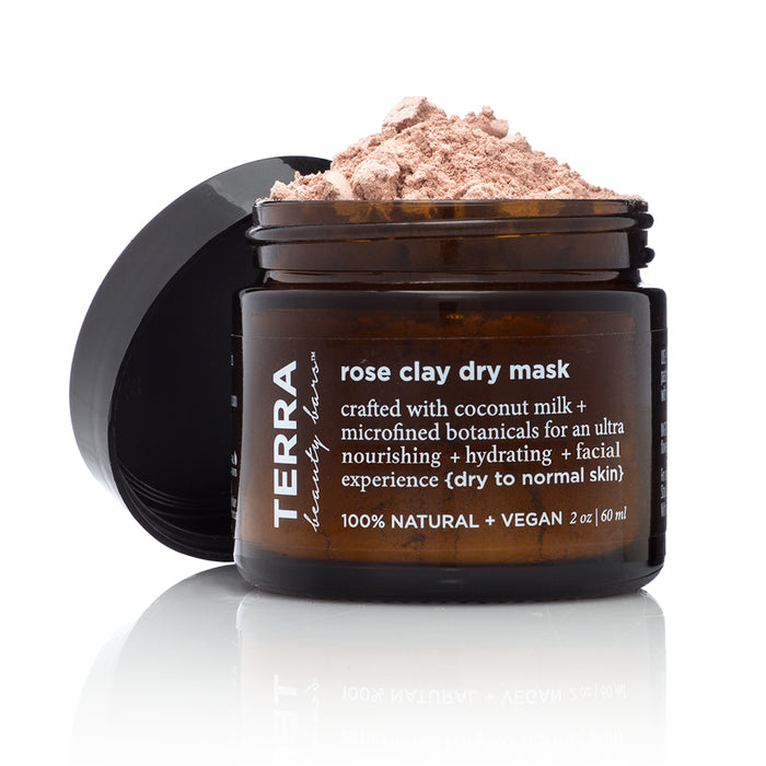 An open jar of Terra Beauty Bars rose clay dry mask with its lid resting beside it, revealing fine pink powder inside. The amber jar label describes it as vegan, natural, and hydrating for dry to normal skin.