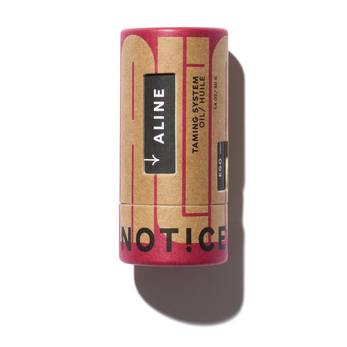 A cylindrical cardboard container labeled ALINE TAMING SYSTEM OIL / HUILE with a kraft and red design, and the partial words NOT:ICE visible near the bottom.