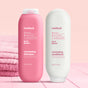 Two bottles of Method hair products on a pink surface: a pink bottle labeled volumizing shampoo and a white bottle labeled volumizing conditioner, both with peony, rose water, and quinoa protein. Folded pink towels are beside them.