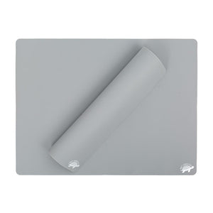 A gray, food-grade silicone baking mat from Net Zero Co.s Reusable Baking Un-Paper collection is laid flat with a corner rolled over. The surface features a small hedgehog logo in the bottom-right corner, providing an eco-friendly alternative to parchment paper.
