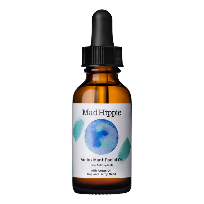 A brown glass dropper bottle labeled Mad Hippie Antioxidant Facial Oil with a white label featuring blue and green abstract art and text listing argan oil, goji, and hemp seed as ingredients.