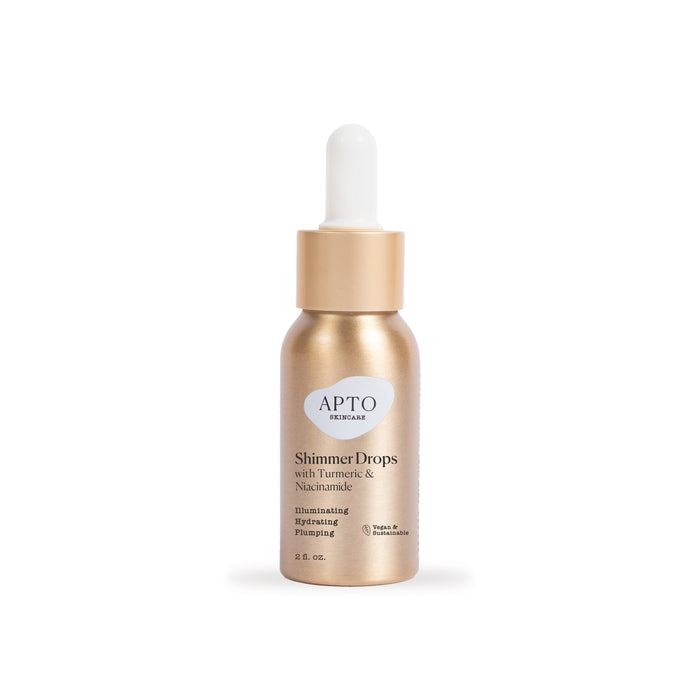 A gold bottle of APTO Skincare Shimmer Drops with a white dropper cap. The label mentions turmeric, niacinamide, and describes the product as illuminating, hydrating, and plumping.