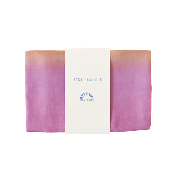 A folded silk fabric transitioning from orange to pink is wrapped with a white label reading Sarahs Silks Giant Playsilk for Open-Ended, Imaginative Play, featuring a small rainbow logo, ideal for Montessori & Waldorf-inspired play.