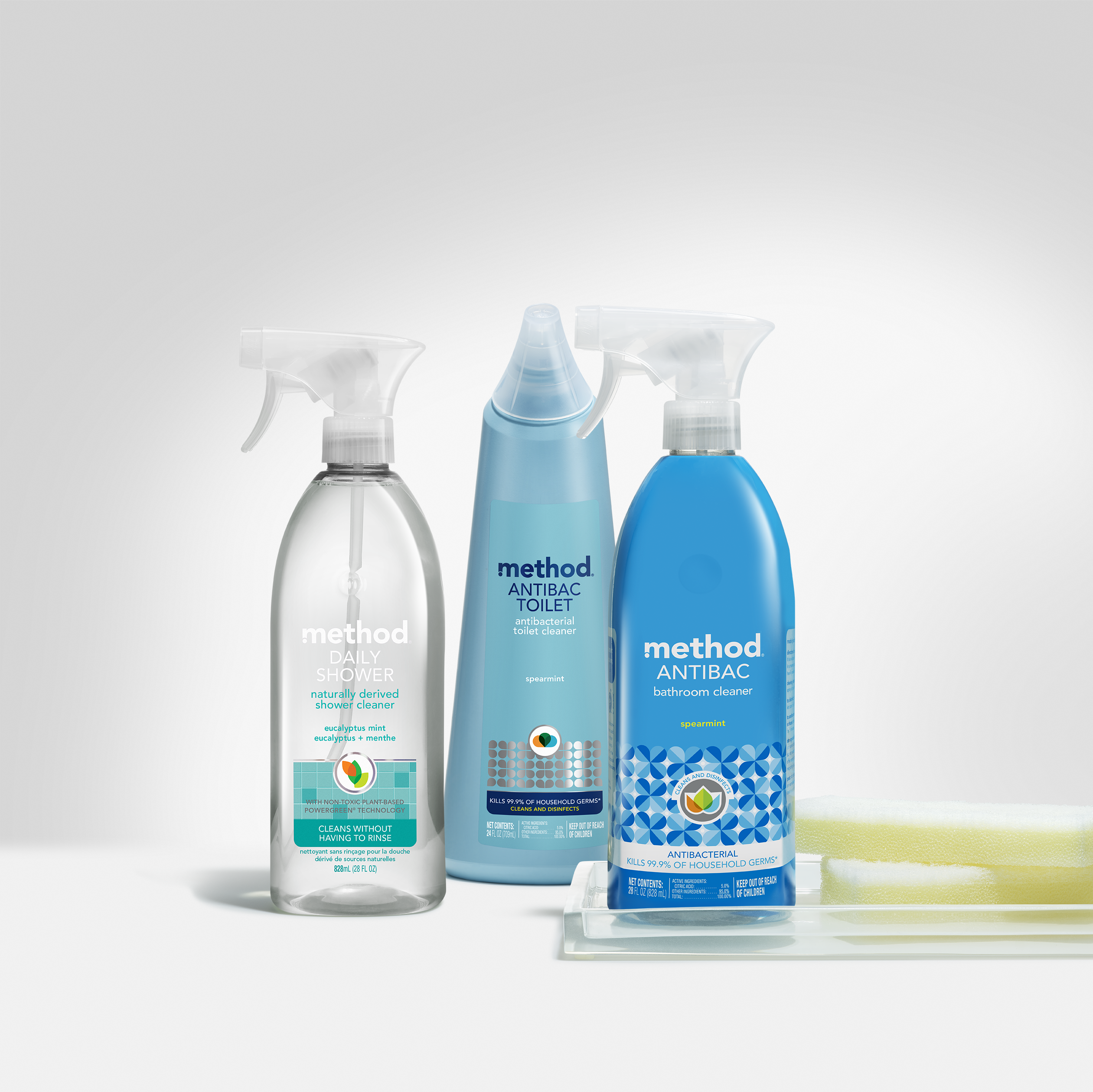 Three bottles, including methods Toilet Cleaner that kills 99.9% of germs, along with a daily shower cleaner and an antibac bathroom cleaner, are neatly arranged with a sponge on a tray against a neutral backdrop.