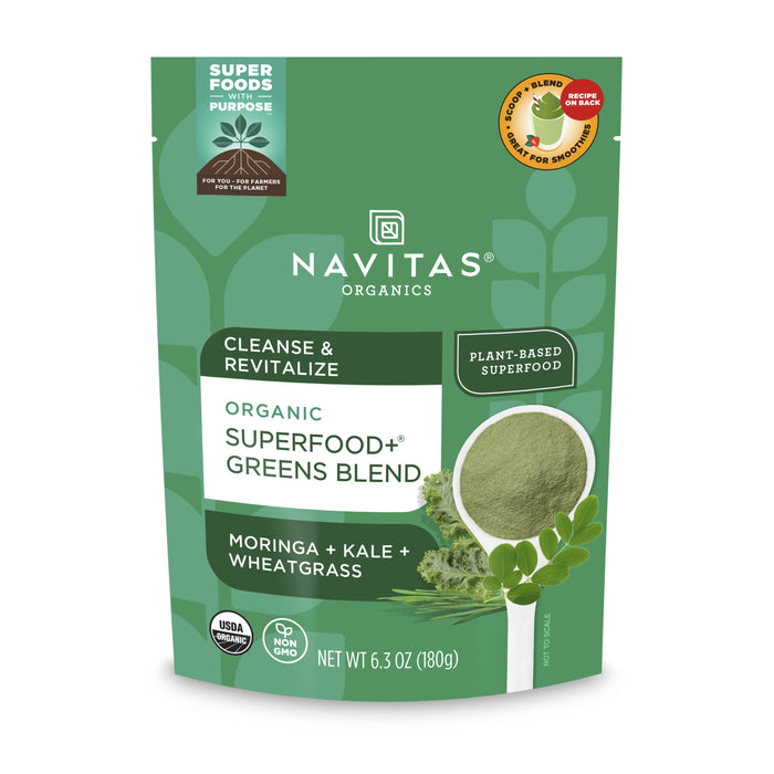 A green pouch of Navitas Organics Organic Superfood+ Greens Blend, featuring images of moringa, kale, and wheatgrass, labeled as plant-based, USDA organic, and weighing 6.3 oz (180g).