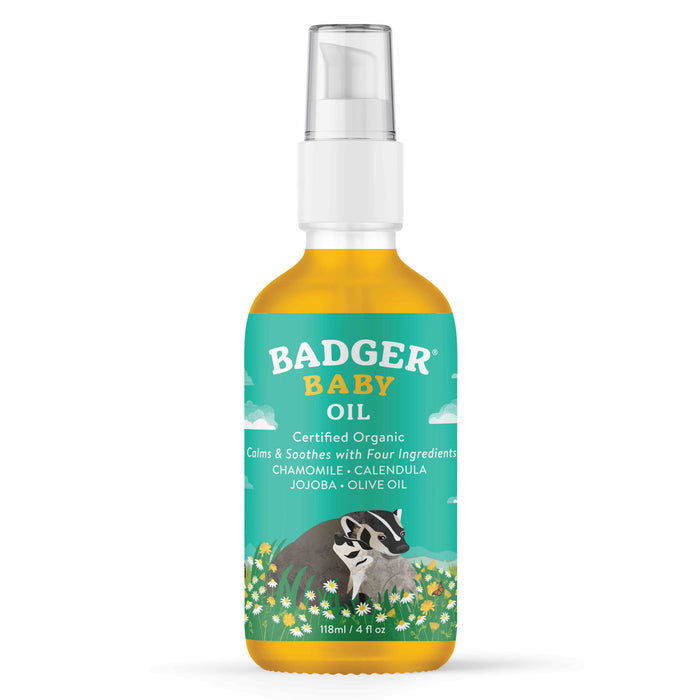A bottle of Badger Baby Oil with a pump dispenser, featuring a colorful label with a badger, flowers, and clouds. The label highlights that it is certified organic and contains chamomile, calendula, jojoba, and olive oil.