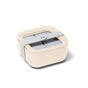 A cream-colored square lunch box with rounded edges, divided into four sections under a lid and secured with a wide, light gray strap across the top.