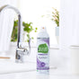 A can of Seventh Generation disinfectant spray sits on a white kitchen counter near a sink, with green plants and white curtains in the background.