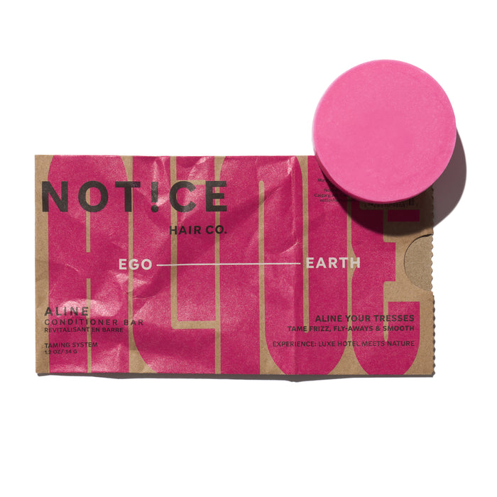 A pink conditioner bar sits next to its brown and pink packaging labeled Notice Hair Co., with the words Ego and Earth and descriptions about taming frizz, smoothing hair, and melting with nature.