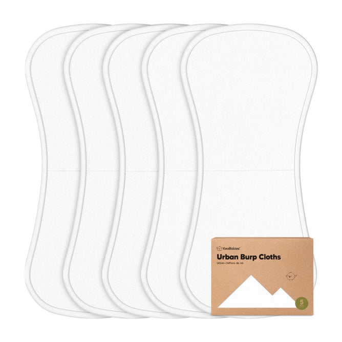 Five white, contoured burp cloths are stacked vertically, with a brown cardboard label in front reading Urban Burp Cloths and featuring a simple mountain graphic.