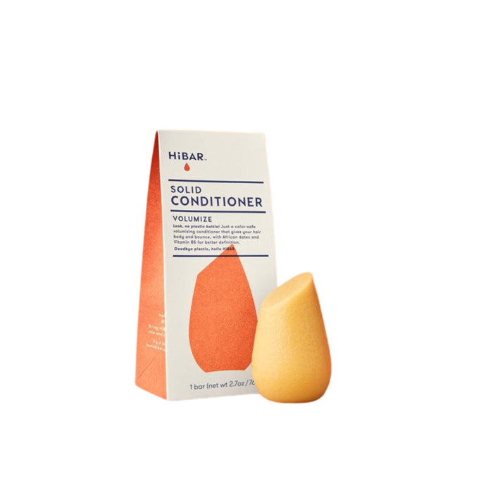 An orange, teardrop-shaped solid conditioner bar stands next to its upright, rectangular HiBAR-branded packaging labeled Solid Conditioner Volumize on a white background.