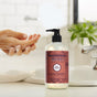 A hand is washed with foamy soap beside a bottle of Mrs. Meyer’s Hand Soap, known for its cruelty-free formula, on a white sink with a plant in the background.