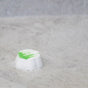 A white shower steamer with a green top sits on a wet shower floor as water sprays down, causing it to fizz and dissolve.