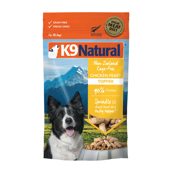 A bag of K9 Natural New Zealand Cage-Free Chicken Feast Topper dog food. The packaging is blue and orange, showing a photo of a happy dog, New Zealand mountains, and chunks of chicken. Text highlights 90% chicken and grain free.