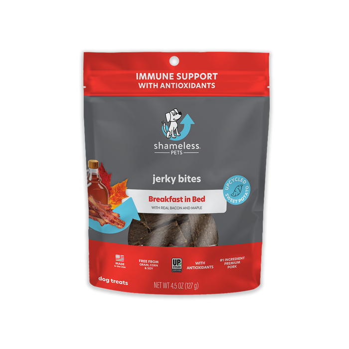 A red and gray bag of Shameless Pets Jerky Bites dog treats labeled Breakfast in Bed with real bacon and maple, showing images of bacon and leaves, and stating Immune Support with Antioxidants.