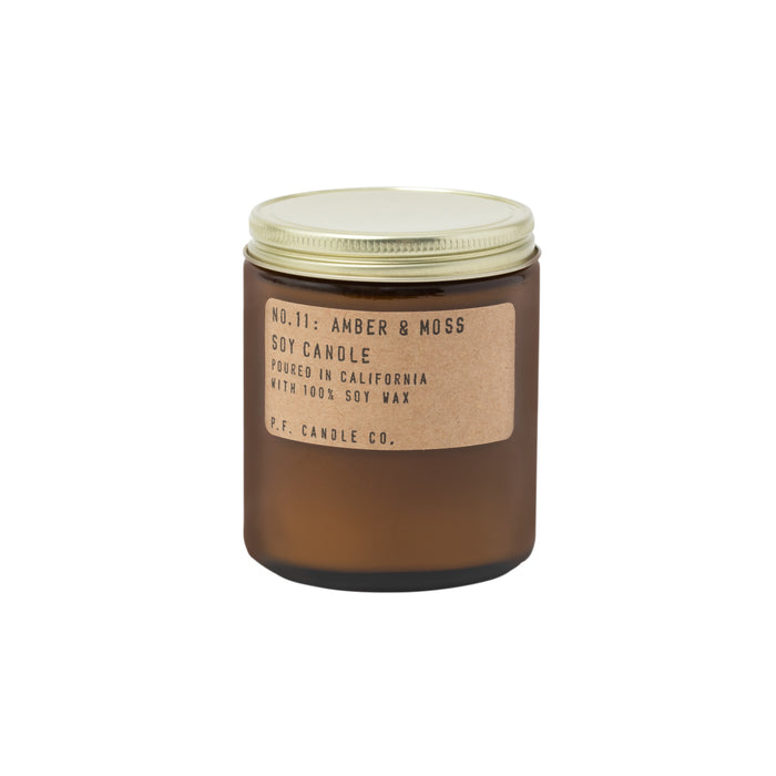 A brown glass jar with a gold lid containing a candle. The label reads: No. 11: Amber & Moss Soy Candle. Poured in California with 100% soy wax. P.F. Candle Co.