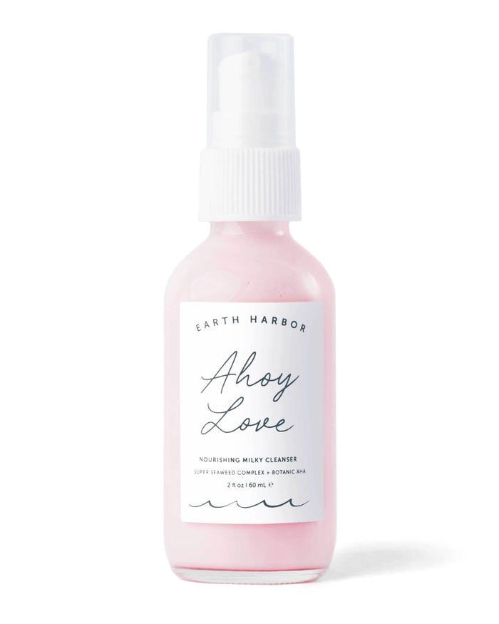 A small clear bottle with a white pump dispenser, containing pink liquid labeled Earth Harbor Ahoy Love Nourishing Milky Cleanser. The label features elegant script and minimalist design.