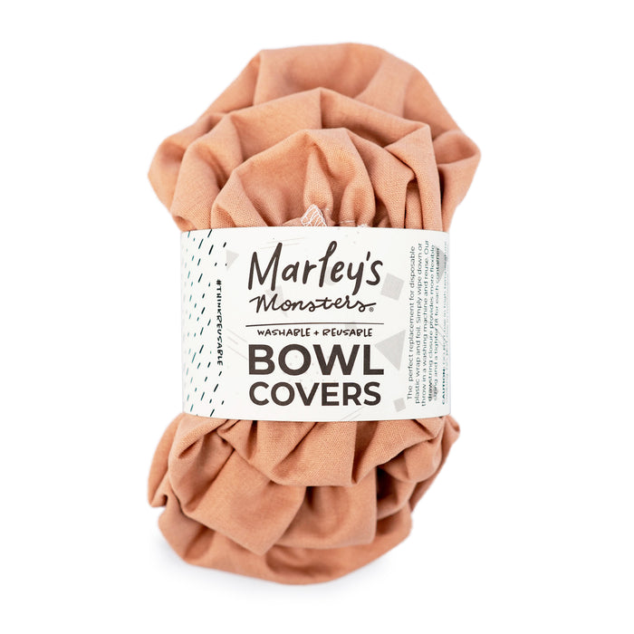 A peach-colored, reusable fabric bowl cover is rolled up with a white label that reads Marleys Monsters Bowl Covers, Washable & Reusable.