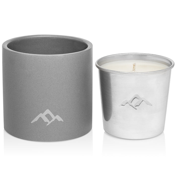A gray cylindrical container and a silver metal candle holder with a white candle inside, both featuring a minimalist mountain logo on the front.