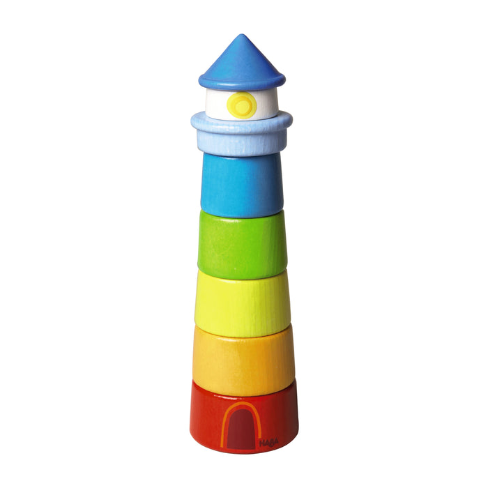 A colorful wooden stacking toy shaped like a lighthouse, with sections in red, orange, yellow, green, blue, and light blue, and a blue cone roof. The base has a small arched doorway.