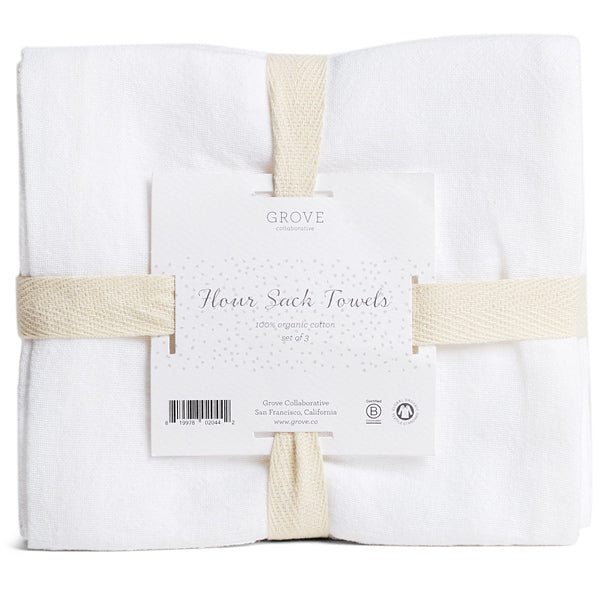 A set of white flour sack towels folded and secured with two beige fabric bands. A label in the center reads Grove Flour Sack Towels, 100% organic cotton, set of 3.