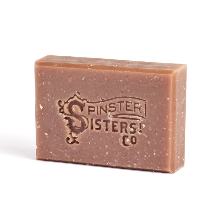 A rectangular bar of brown soap embossed with the logo Spinster Sisters Co. sits on a white background. The soap has a slightly speckled texture.