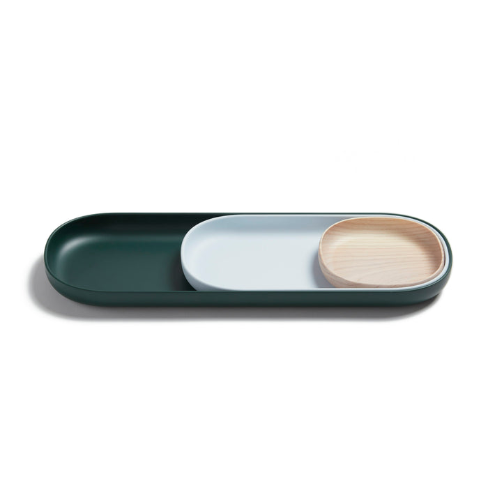 A modern, minimalist tray set with three nesting dishes: a large dark green tray, a smaller white tray, and a round light wooden bowl, arranged neatly on a white background.