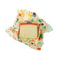 A wedge of cheese with a reddish rind rests on a Bees Wrap Assorted 3 Pack Holiday wrap, decorated with colorful animal and plant designs, keeping food fresh and plastic free—all set against a white background.