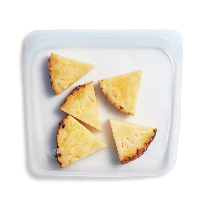 Five triangular slices of pineapple are arranged inside a clear, reusable silicone storage bag on a white background.